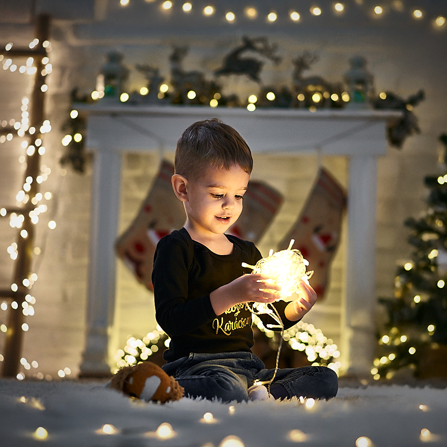 Karácsonyi díszlet fényfüzérrel, kisgyerek ünnepi hangulatban.